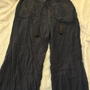 Svarta vida byxor med snörning H&M - Svarta, vida byxor från H&M i storlek 46. Byxorna har resår i midjan och snörning med tofsar framtill. Tillverkade i ett lätt och mjukt tyg som ger en avslappnad känsla. Använda ett par gånger.