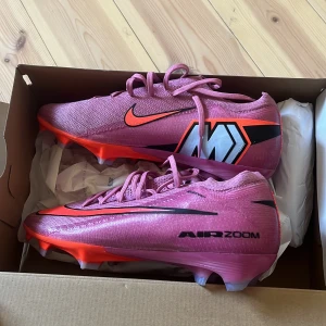 Nike Mercurial Air Zoom fotbollsskor rosa strl 41 - Säljer ett par Nike Mercurial Air Zoom fotbollsskor i en snygg rosa färg med svarta och neonröda detaljer. Skorna har snörning, platt sula med dobbar och är tillverkade i syntetmaterial. Perfekta för dig som vill sticka ut på planen! Köpte för 2500 säljer för 2000 använt de en träning de är lite för stora för mig finns påse och box till
