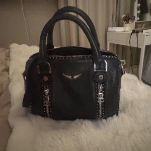  Zadig & Voltaire väska, med silverdetaljer - Cool svart handväska från Zadig i skinn med silverfärgade dragkedjor och nitar. Väskan har både handtag och en avtagbar axelrem med vadderad del för extra komfort. Snygg metall-logga framtill och flera fack med dragkedja. Pris kan diskuteras vid snabb affär💗💗💗