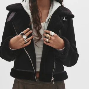 Svart teddyjacka från Pull&Bear - Svart teddyjacka med bred krage, dragkedja och detaljer i fuskpäls. Jackan har två fickor med dragkedja, spänne vid kragen och croppad passform. Perfekt för dig som vill ha en snygg och trendig look med lite edge.                                  .     .                                                                                             Vill även  lägga tilll att den är liten i storlek, själv har jag storlek M kan hända att jag har S.