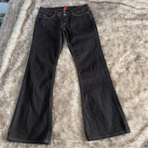 Svarta low waist bootcut jeans från Vila - Svarta jeans med låg midja från Vila med bootcut-modell och kontrastsömmar. Klassisk femficksdesign och dragkedja i gylfen. Jeansen har en snygg passform med utsvängda ben och är tillverkade i ett slitstarkt bomullsmaterial.