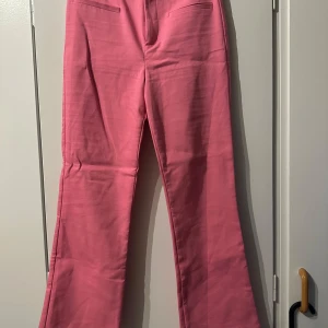 Rosa bootcut byxor från Zara - Snygga rosa bootcut-byxor från Zara med hög midja och dragkedja framtill. Byxorna har raka ben som slutar i en lätt utsvängd siluett och är tillverkade i ett mjukt bomullsmaterial. Perfekta för dig som vill sticka ut med färg.