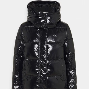 Svart pufferjacka från Calvin Klein - Snygg svart pufferjacka från Calvin Klein med glansig finish och diskret CK-logo på bröstet. Jackan har hög krage, huva och dragkedja framtill. Perfekt för kalla dagar när du vill hålla stilen och värmen. Använd 1 vinter och är i mycket bra skick! Finns en mindre defekt som syns på andra bilden, men inget som läggs märke till vid användning. Pris går att diskuteras vid snabb affär. Storlek xl men liten i storlek så den sitter som m! Nypris är runt 2400kr!
