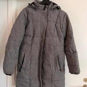 Grå dunjacka från Take Off XS - Snygg grå dunjacka från Take Off i storlek XS. Jackan har huva, långa ärmar och dragkedja framtill med knappar. Praktiska fickor på sidorna och en stilren, enkel design som passar perfekt för kalla dagar. Priset kan diskuteras 