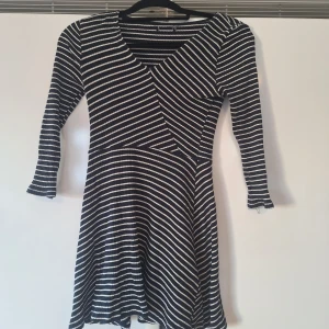 Marinblå randig klänning med v-ringning - Snygg marinblå klänning med diagonala ränder och v-ringad hals. Klänningen har långärmade ärmar och är tillverkad i ett mjukt, ribbat material som ger en skön passform. Kjolen är lätt utsvängd och längden är kort, perfekt för dig som gillar en stilren look.