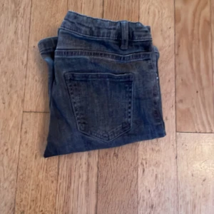 Bootcut jeans från Kappahl, stl 134 - Snygga mörkgrå bootcut jeans från Kappahl i klassisk denim. Jeansen har fem fickor, bälteshällor och knapp med texten 'DENIM'. Perfekta för dig som gillar en lite vidare passform nertill och vill ha en cool vardagslook.