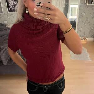 Vinröd stickad polotröja med kort ärm - Säljer en vinröd stickad polotröja med korta ärmar och bred, mysig krage. Tröjan är croppad och har ribbade detaljer vid ärmslut och nederkant. Perfekt för dig som gillar en chill och trendig look med lite edge.