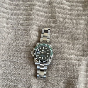  klocka svart/grön stål - En elegant och iögonfallande herrklocka som kombinerar stil och funktion perfekt. 	•	⌚ Automatisk urverk (ingen batteri, drivs av rörelse) 	•	🟢⚫ Svart urtavla med svart/grön vridbar bezel 	•	🔧 Boett och armband i rostfritt stål 	•	📆 Datumvisning 	•	🌊 Tålig mot stänk – passar för vardagsbruk 	•	🔒 Viklås med säkerhetsfunktion 	•	📏 Justerbar länk – passar de flesta handleder