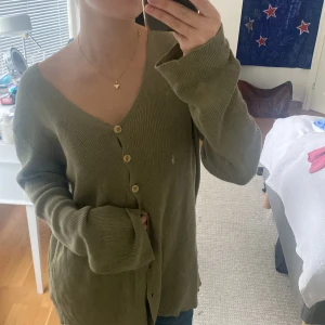 Olivgrön kofta med knappar - Olivgrön ribbstickad kofta från Benetton med v-ringning och träfärgade knappar. Långärmad och loose fit, mysig till hösten
