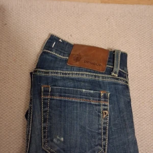 Blå jeans från Dondup - Snygga blå jeans från Dondup med klassisk femficksdesign och kontrastsömmar. Jeansen har en läderpatch med logga bak i midjan och metallknapp framtill. Perfekta för dig som gillar en stilren och tidlös look. W27