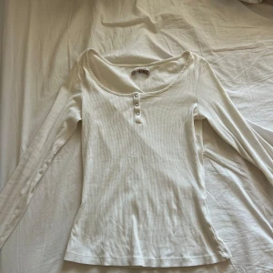 Vit ribbad långärmad topp Anna Field - Säljer en vit ribbad långärmad topp från Anna Field med snygg u-ringning och tre knappar framtill. Modellen är figurnära och har en mjuk, stretchig känsla som passar perfekt till jeans eller kjol. Knappt använd💓