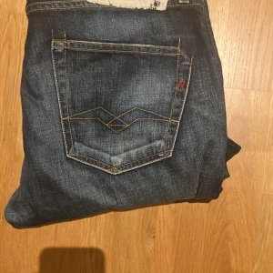 Mörkblå Replay jeans, straight fit - Säljer ett par mörkblå jeans från Replay med klassisk femficksdesign och snygga kontrastsömmar. Jeansen har raka ben och subtila slitningar för en cool look. Materialet är robust denim och passformen är normal. Perfekta för dig som gillar stilrena jeans med detaljer.