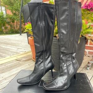 Svarta höga stövlar från Bianco - Snygga svarta stövlar från Bianco med spetsig tå och hög klack. Tillverkade i skinn med dragkedja på insidan och stilrena sömdetaljer längs skaftet. Köpta på 90-talet. Defekt förkommer vid blixtlåset på bild 4. 