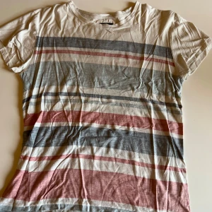 Randig t-shirt från Crocker XS - Snygg t-shirt från Crocker i storlek XS med breda horisontella ränder i vitt, grått och rött. T-shirten är kortärmad och har en klassisk rund halsringning. Tillverkad i mjuk bomull, perfekt för en avslappnad stil.