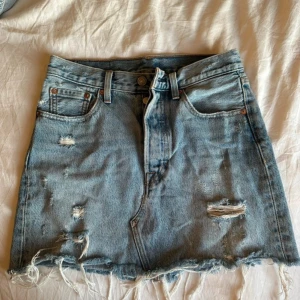 Levi's ljusblå jeanskjol med slitningar - Ljusblå jeanskjol från Levi's med rå kant och slitna detaljer framtill och baktill. Kjolen är ljusblå, den rätta färgen framhävs på sista bilden.