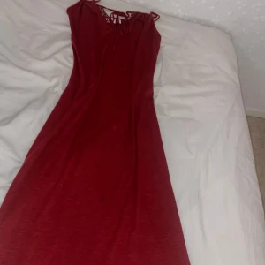 Röd långklänning med snörning - Snygg röd långklänning med smala axelband och snörning upptill. Klänningen har en enkel, rak passform och är ärmlös. Perfekt för dig som vill ha en stilren och bekväm look med en liten twist vid halsen.