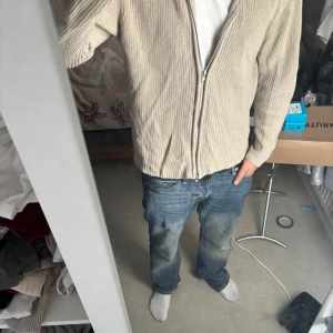 Beige stickad kofta med dragkedja Lager 157 - Beige stickad kofta från Laget 157 med hel dragkedja framtill och krage. Tröjan har långärmad passform och är gjord i mjuk bomull. Perfekt för lager-på-lager och chill stil. Enkel att matcha med jeans eller andra byxor.