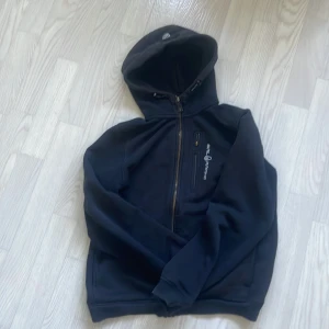 Svart hoodie från Sail Racing - Svart hoodie/zip från Sail Racing med ett litet lagat jack som man inte märker till.