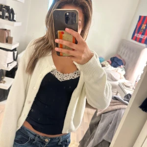 Vit stickad kofta med knappar - Mysig vit stickad kofta med långa ärmar och knappar framtill. Koftan har en klassisk, enkel design och är perfekt att slänga över en topp. Ribbstickade muddar vid ärmslut och nederkant ger en snygg touch.