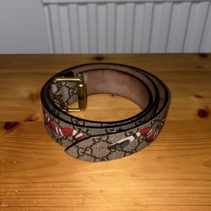 Gucci GG Supreme bälte med orm -  Äkta Gucci bälte. Bältet är flexibelt och unikt och perfekt för dig som vill ha ett stilrent och exklusivt accessoar till din outfit.