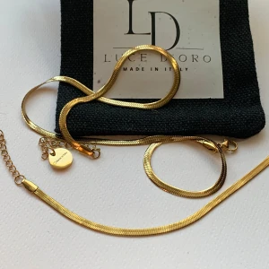 Guldpläterat halsband & armband Luce D'Oro - Säljer ett snyggt set med halsband och armband från Luce D'Oro, tillverkade i Italien. Båda är i guldpläterat rostfritt stål med en platt, ormliknande kedja som ger en clean och modern look. Perfekt för dig som gillar stilrena smycken med guldfinish.