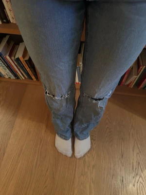 Blå raka jeans med slitna knän - Säljer ett par blå jeans med raka ben och slitna detaljer vid knäna. Jeansen har klassisk femficksdesign och är tillverkade i jeansmaterial. Perfekta för en avslappnad och trendig look. Strl 158.