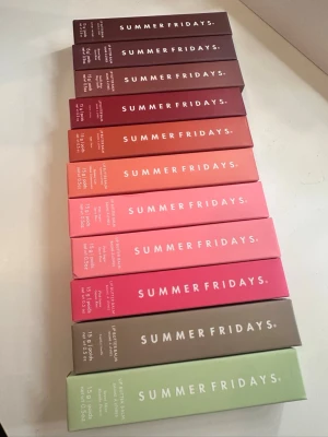 Summer Fridays Lip Butter Balm styck pris - Säljer ett set med Summer Fridays Lip Butter Balm i 10 olika färger. Förpackningarna är i nyanser av brunt, rött, orange, rosa, grönt och beige. Varje tub innehåller 15g och är designad i en stilren kartong med vit text. Perfekt för dig som vill ha mjuka och återfuktade läppar. 