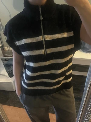 Randig stickad tröja från Zara - Säljer en svart och vit randig stickad tröja från Zara. Tröjan har half zip-dragkedja framtill, hög krage och korta ärmar. Super mjuk kvalitet!