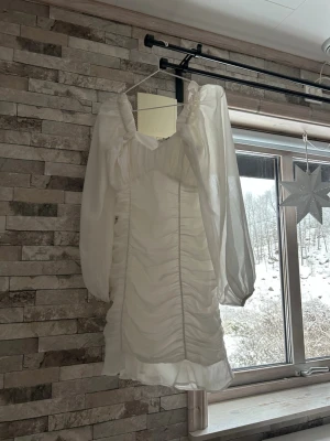 Vit kortklänning från NLY Trend - Supersöt vit kortklänning från NLY Trend med puffiga långärmar i transparent tyg och snygg rynkad effekt framtill. Klänningen har v-ringad urringning och dragkedja i sidan för enkel påklädning. Perfekt för dig som vill sticka ut lite extra!