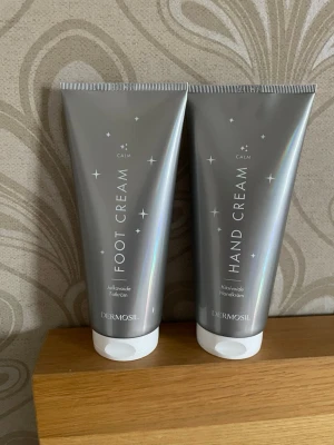 Handkräm & fotkräm Dermosil 200ml - Säljer ett set med handkräm och fotkräm från Dermosil, båda i silvriga tuber på 200 ml. Vegansk formula och mild doft. Tuben har en modern, stilren design med vita detaljer och stjärnmotiv. Perfekt för dig som vill ha återfuktade händer och fötter.
