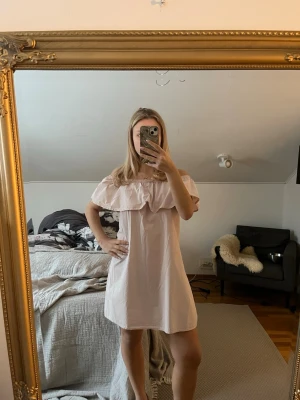 Ljusrosa offshoulder kortklänning - Supersöt ljusrosa kortklänning med offshoulder och volang upptill. Klänningen har en avslappnad passform och är gjord i ett tunt, mjukt bomullstyg. Perfekt för varma dagar och ger en romantisk vibe.