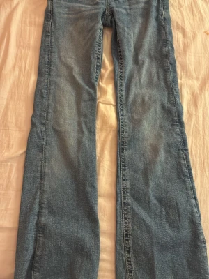 Blå bootcut jeans Gina Tricot 152 - Säljer ett par ljusblå bootcut jeans från Gina Tricot i storlek 152. Jeansen har snygga detaljer på bakfickorna med knappar och broderade sömmar. Klassisk femficksmodell i mjukt denimtyg, perfekta till en avslappnad look.