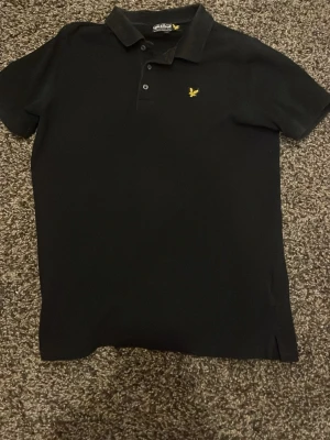 Svart pikétröja från Lyle & Scott - Riktigt fet svart pikétröja från Lyle & Scott med gul broderad logga på bröstet. Storlek xs/s. 