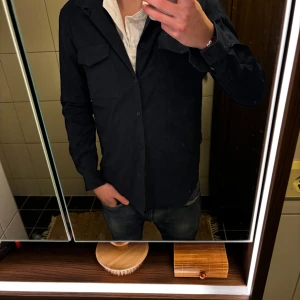 Mörkblå overshirt från Zara - Snygg mörkblå overshirt från Zara med klassisk krage och två bröstfickor med lock. Skjortan har knäppning framtill och är långärmad. Perfekt att bära öppen över en t-shirt eller stängd för en clean look.