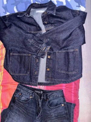 Mörkblå jeansjacka med stora fickor - Säljer en mörkblå jeansjacka från ZARA med klassisk krage, stora framfickor och kontrastsömmar. Jackan har knappar framtill och långa ärmar med knapp vid ärmslut. Perfekt för dig som gillar en enkel men snygg denimlook.