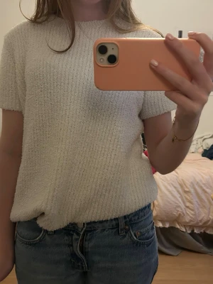 Vit ribbad kortärmad topp - Mysig vit topp med ribbad struktur och korta ärmar. Toppen har en rak passform och är tillverkad i ett mjukt, stickat material som känns skönt mot huden. Perfekt att styla med jeans eller kjol för en enkel och fräsch look. 