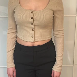 Trendig beige croppad topp i XS från SHEIN - •Trendig beige croppad topp i XS från SHEIN med långa ärmar och snygga knappar framtill.       •Toppen är ribbad och har en rundad halsringning.                            •Oanvänd.                                                  •Modellen: ca 1.60 & har XXS i strl.