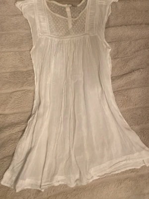 Vit kortklänning i bomull - Luftig vit kortklänning i tunn bomull med broderade detaljer upptill och lätt rynkad kjol. Perfekt för varma dagar och ger en romantisk vibe. Klänningen har en enkel, flowy siluett och känns superfräsch och somrig. Etiketten är bortklippt och vet tyvärr inte märket.💕