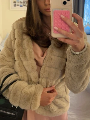 Beige pälsjacka i fluffigt material - Supermjuk och fluffig beige pälsjacka med breda, markerade sömmar. Den är långärmad och har en lyxig look som lyfter vilken outfit som helst.