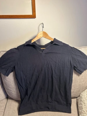 Svart kortärmad polotopp i bomull S - En svart polotopp i storlek S med korta ärmar och klassisk krage. Toppen är tillverkad i mjuk bomull och har en enkel, stilren design utan mönster eller detaljer. Perfekt för en clean och avslappnad look.