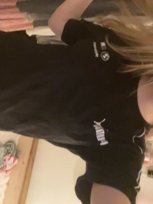 Svart Puma BMW Motorsport t-shirt - Säljer en svart Puma t-shirt i samarbete med BMW Motorsport. T-shirten har vita loggor på bröstet och tunna vita detaljer längs axlarna. Klassisk passform och rund hals. Perfekt för dig som gillar motorsport och streetwear.