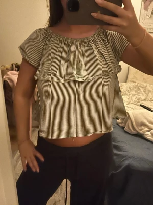 Randig volangtop  - Säljer en superfin randig topp med volangdetalj. Toppen är vit med svarta smala ränder och kan bäras på flera sätt: offshoulder, oneshoulder eller axelbandslös. Luftig och croppad modell i mjuk bomull, perfekt för varma dagar.