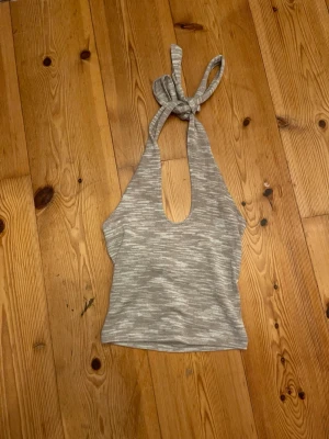 Grå ribbad halterneck topp H&M Divided - Säljer en gråmelerad ribbad halterneck topp från H&M Divided i storlek S. Toppen har breda band som knyts i nacken och är ärmlös med en djup urringning. Perfekt till sommaren och enkel att styla med jeans eller kjol.