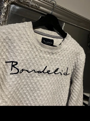 Vit sweatshirt från Bondelid - Säljer en vit sweatshirt från Bondelid med cool struktur i tyget och svart broderad logga över bröstet. Tröjan har rund halsringning och långa ärmar. Perfekt för dig som gillar stilrena och bekväma plagg.