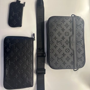 Louis Vuitton svart axelväska i skinn, kvitto finns!! - Säljer en svart axelväska från Louis Vuitton i skinn med klassiskt monogrammönster. Väskan har justerbar axelrem, matchande plånbok och pouch, allt i samma stilrena design. Perfekt för dig som vill ha en lyxig och snygg accessoar. Använd bara en sommar, pris kan diskuteras 
