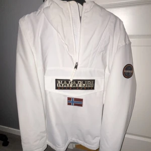 Vit vindjacka från Napapijri - Säljer en snygg vit vindjacka från Napapijri. Perfekt för vintern och en jätte fin vit färg som lyser ute i snön, och den är i helt nytt skick där jag bara använt den 2-3 gånger för att jag hittat en annan jacka till mig själv.