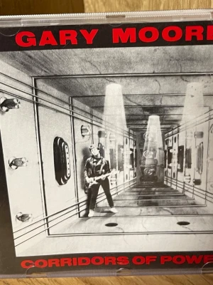 Gary Moore - Corridors of Power CD - Upptäck Gary Moores 'Corridors of Power' – en ikonisk musikupplevelse med kraftfulla gitarrsolon och låtar som 'Rockin' Every Night' och 'Always Gonna Love You'. Perfekt för dig som älskar rock och vill ha energi och känsla i din samling!