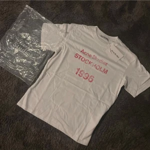  Acne Studios 1996 t-shirt  - Säljer en clean vit t-shirt från Acne Studios med rött tryck framtill där det står 'Acne Studios STOCKHOLM 1996'. Klassisk rund hals och korta ärmar. Kommer med originalpåse och tag kvar. 