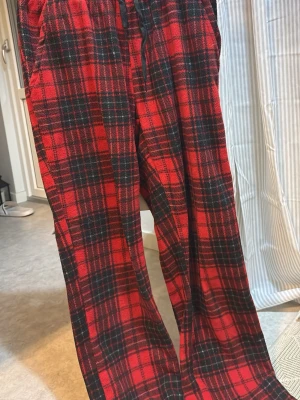 Röda rutiga mjukisbyxor - Säljer ett par röda mjukisbyxor med svart rutigt mönster. Byxorna har resår i midjan och är i ett mjukt och skönt material! Aldrig använda, går ut lite nedtill! 
