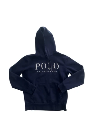 Ralph Lauren Hoodie - Snygg och bekväm Polo Ralph Lauren hoodie i mörkblått. Klassisk design med ikoniskt POLO-tryck på bröstet. Mjuk och skön kvalitet med huva, känguruficka och bra passform. Perfekt till vardags – både stilrent och avslappnat.